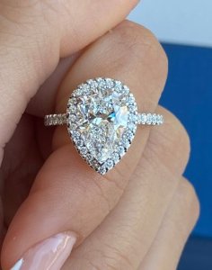 Pear-shaped diamond engagement ring with halo and pavé-set shoulders in platinum.